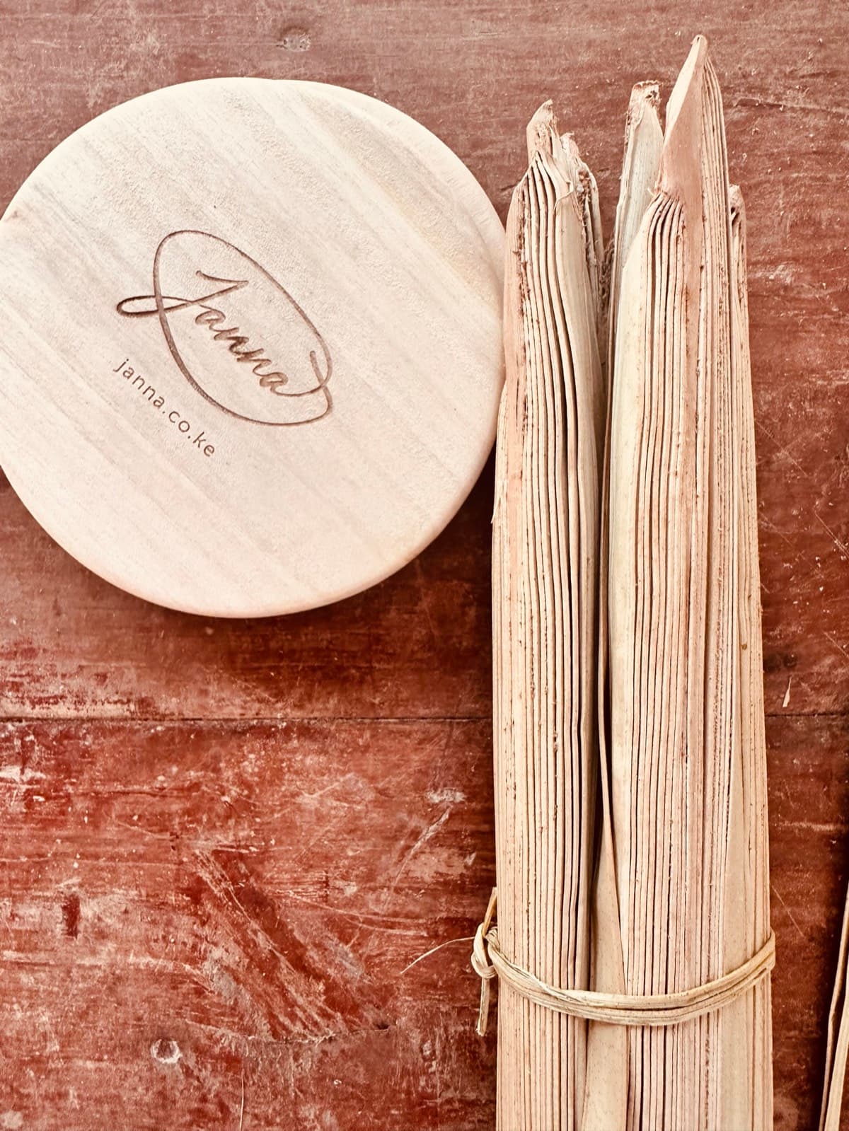 Janna-branded wooden lid disc alongside a bundle of raw dried palm strips